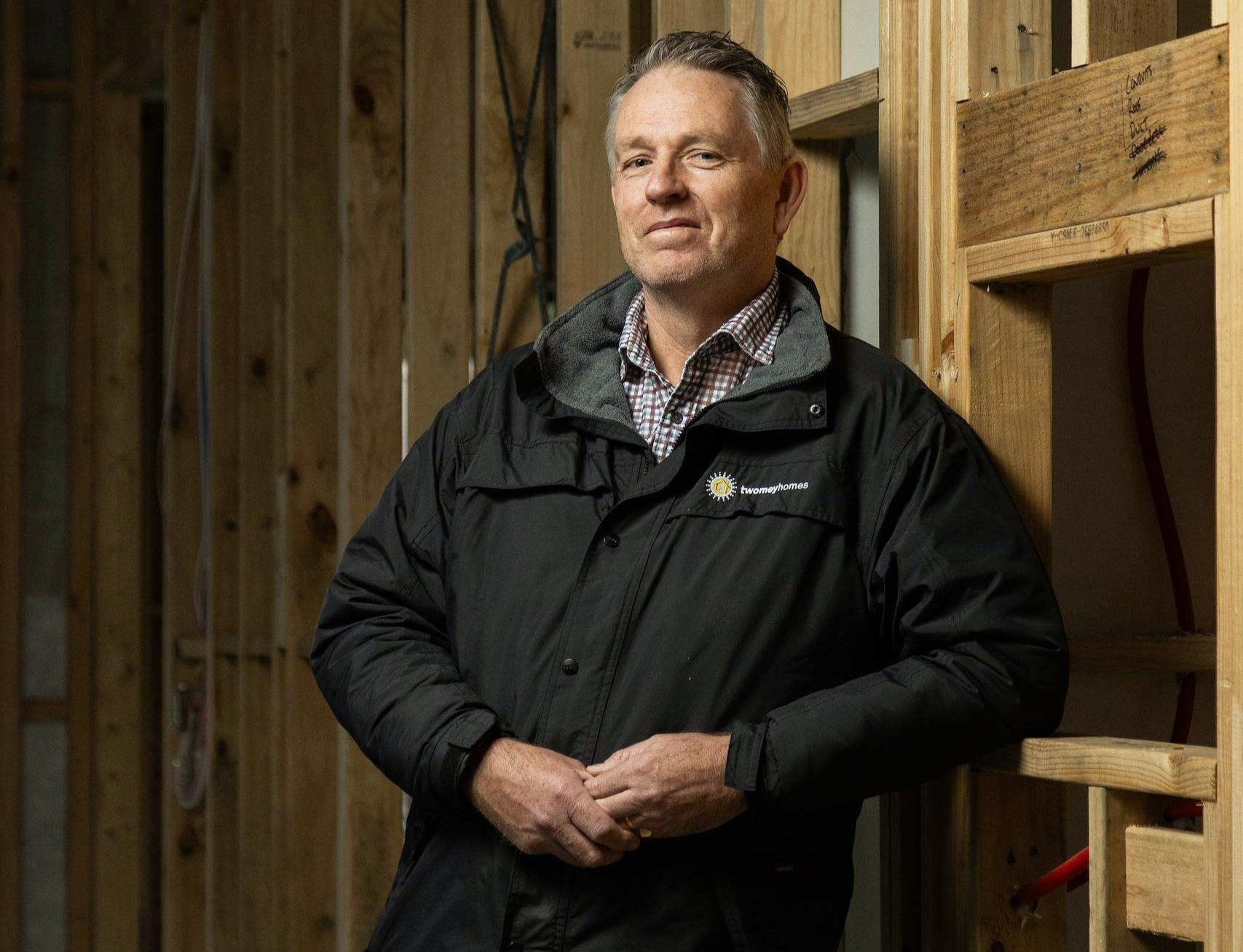 Man in a black jacket standing in a wooden barn interior, hands clasped, looking ahead — Twomey Homes in Delacombe, VIC