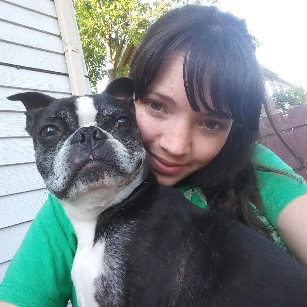 A woman in a green shirt is holding a black and white dog
