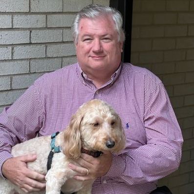 A man in a pink shirt is holding a small dog.