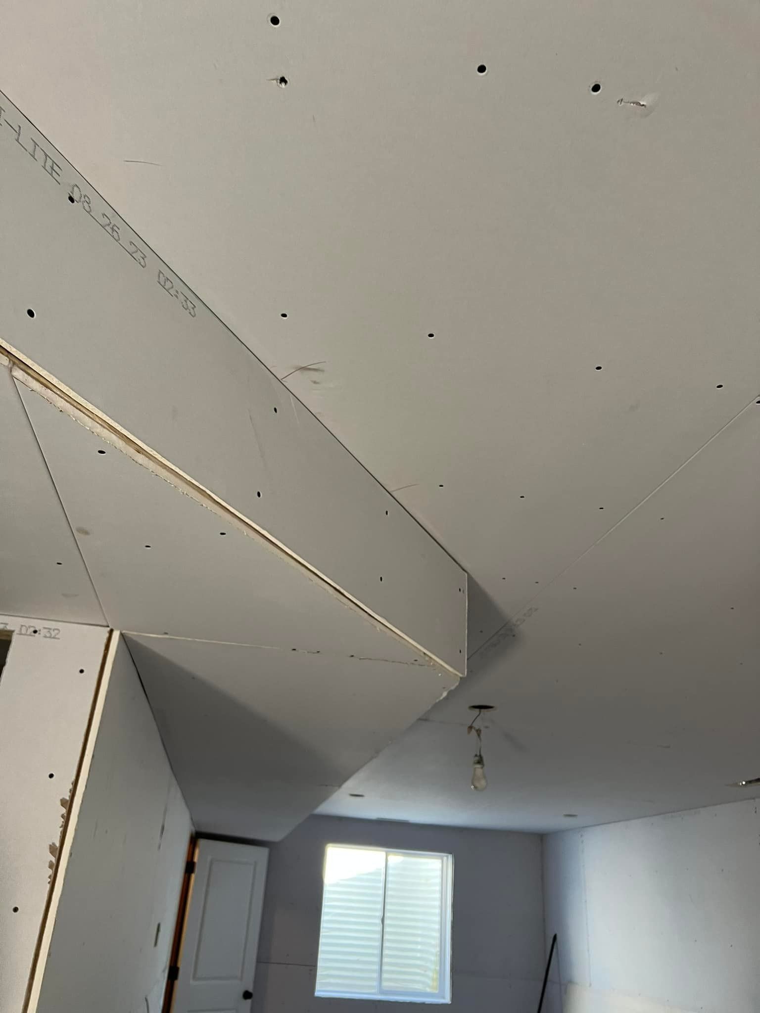 Drywall installation in a room with a sloped ceiling and window, visible screw holes.