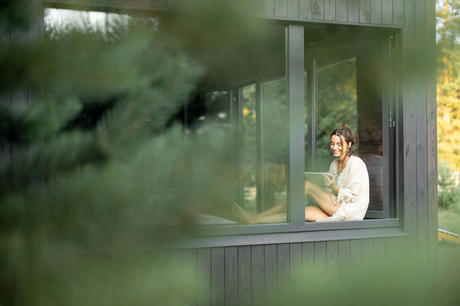 woman resting at beautiful country house or hotel, sitting with tablet on the window