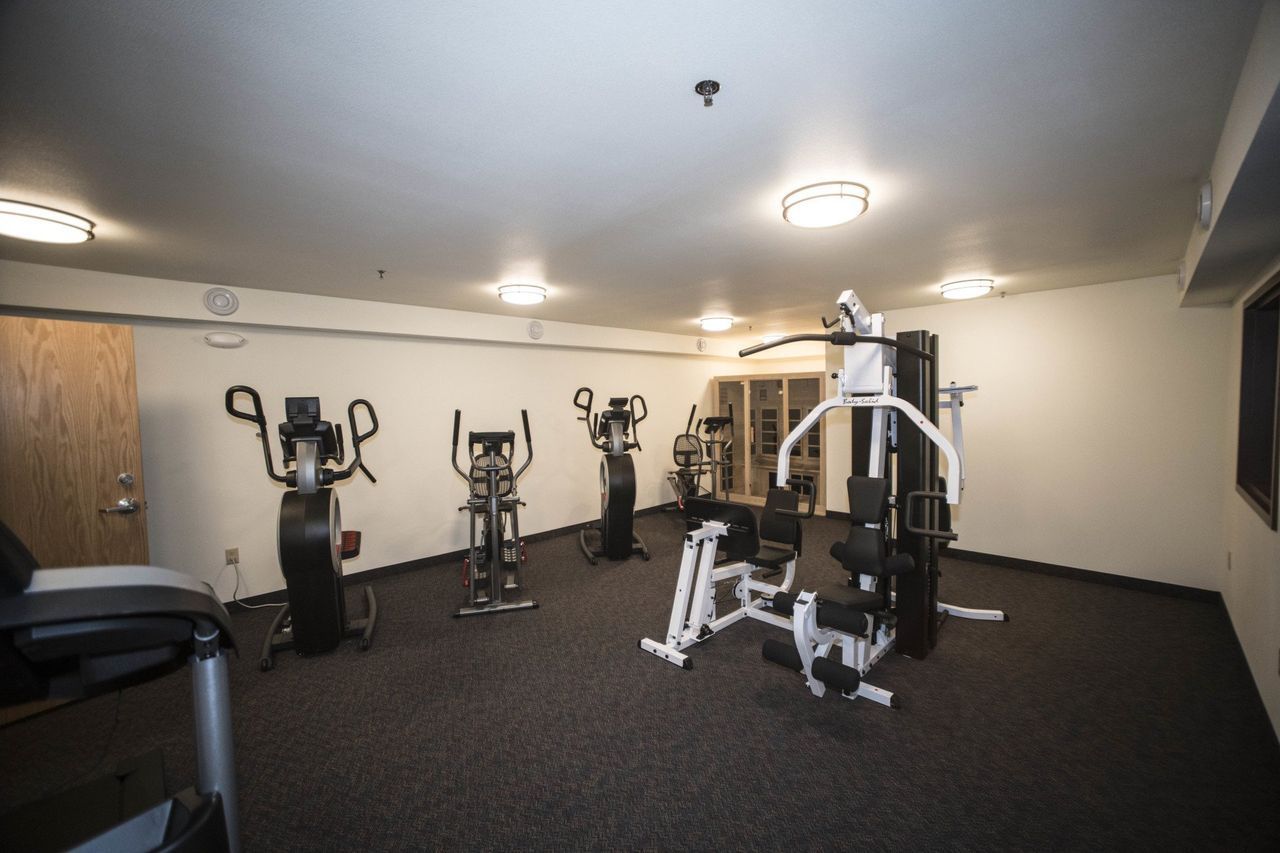 Gym | Healy, AK | Denali Totem Inn Gym interior with exercise equipment on a dark carpeted floor. Ellipticals and a multi-station machine are visible.