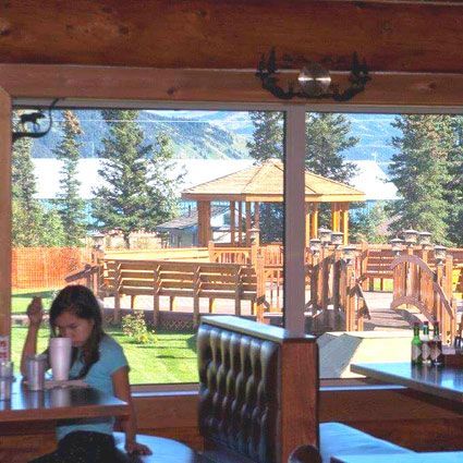 A woman sits at a table in a restaurant, looking out at a lakeside gazebo and deck.