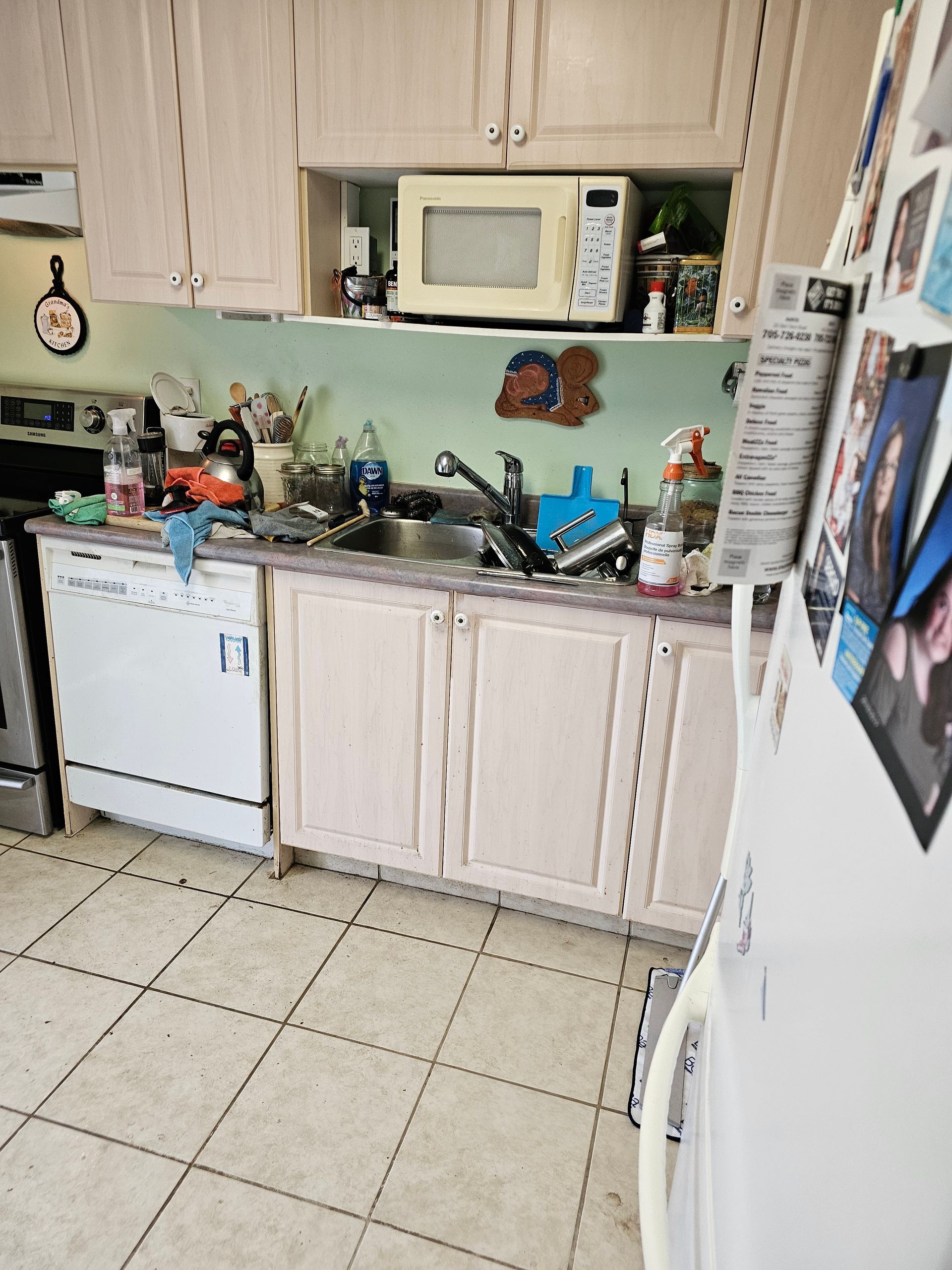 Small kitchen with white cabinets, sink, microwave, refrigerator, and tiled floor.