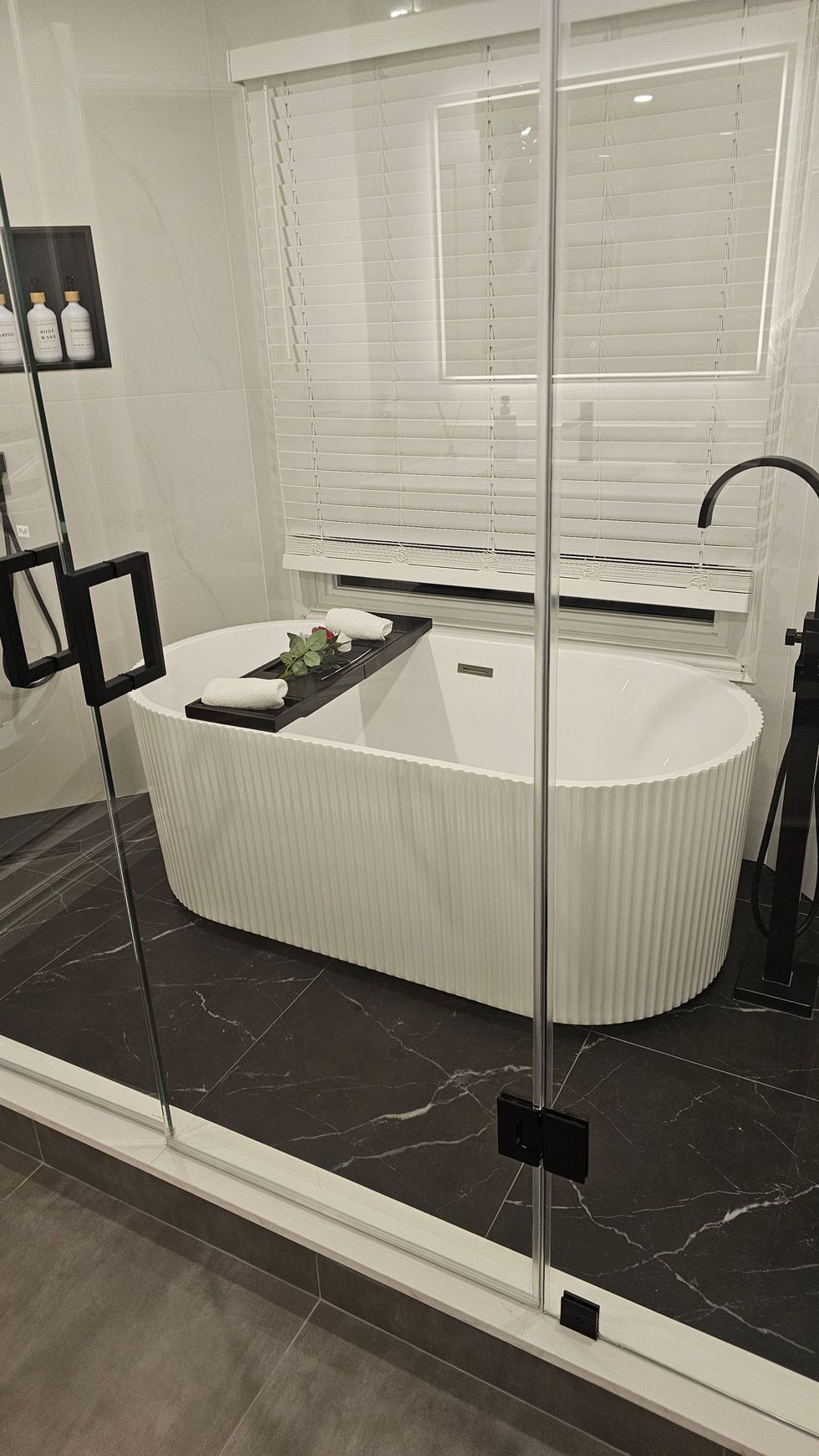 Modern bathroom with a white freestanding tub, dark tile floor, and glass shower doors overlooking the space