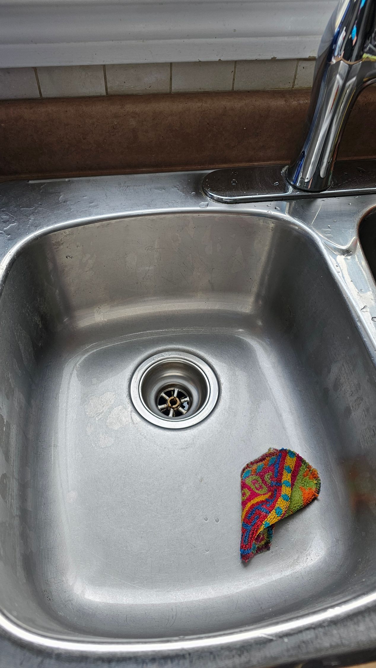 Stainless steel kitchen sink with a colorful scrub sponge in the basin.