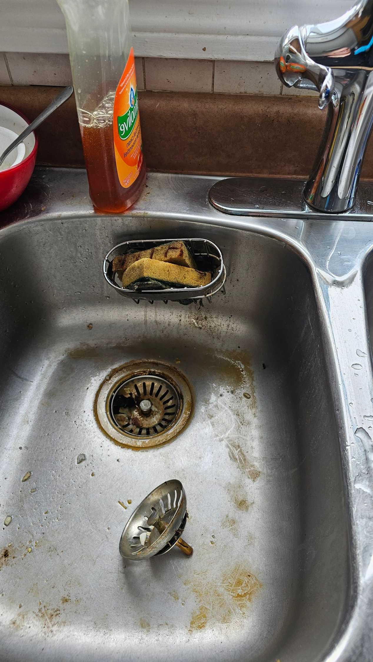 Dirty kitchen sink with food debris, a sponge, and a faucet beside it