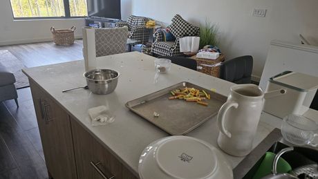 Messy kitchen island with dishes, pot, tray of food scraps, and a white pitcher