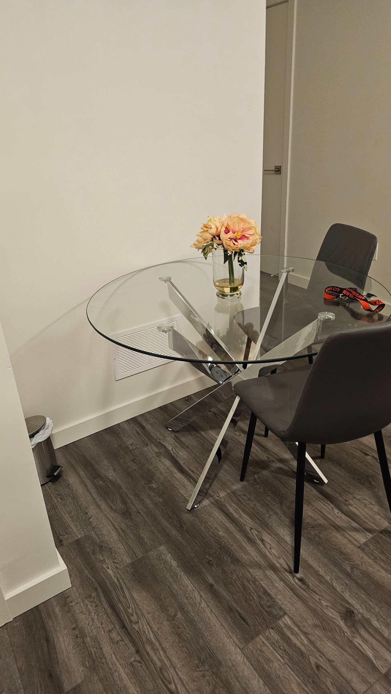 Small dining nook with a round glass table, two black chairs, and a vase of flowers by a wall.