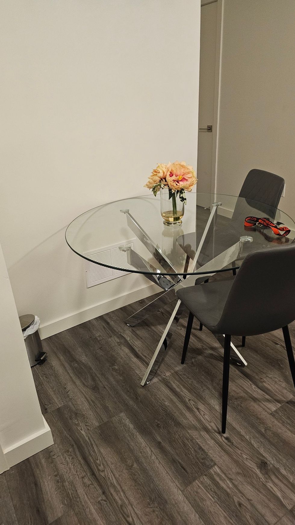 Small glass dining table with black chairs, a vase of flowers, and an open laptop in a corner.