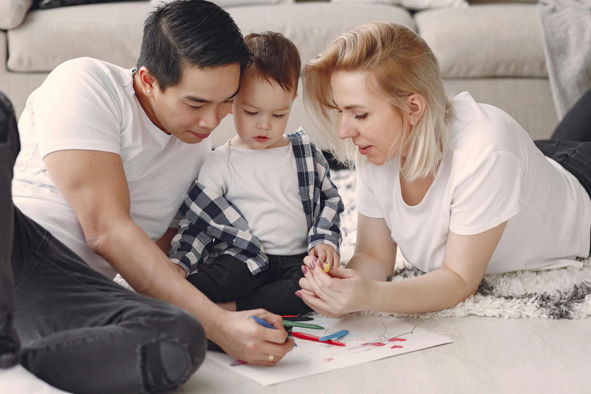 Three people on a couch drawing together on a sheet of paper with colored markers