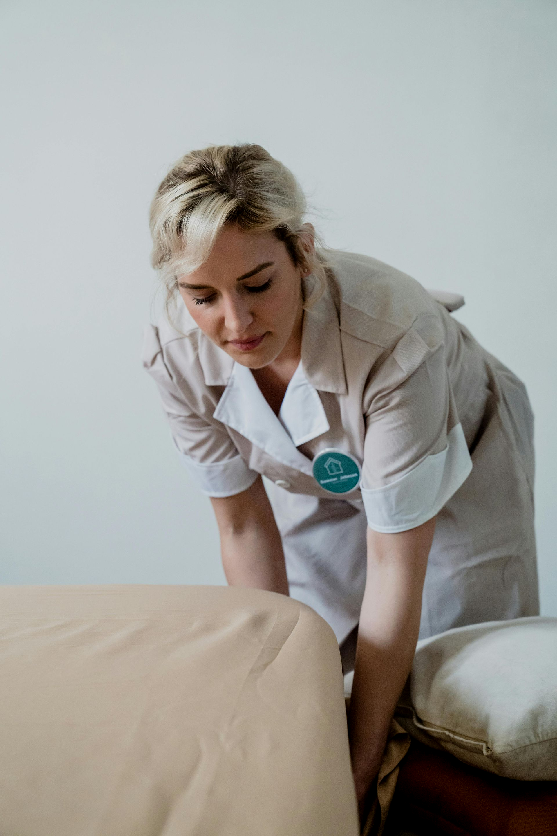 Care worker leaning over a bed, adjusting bedding in a bright room