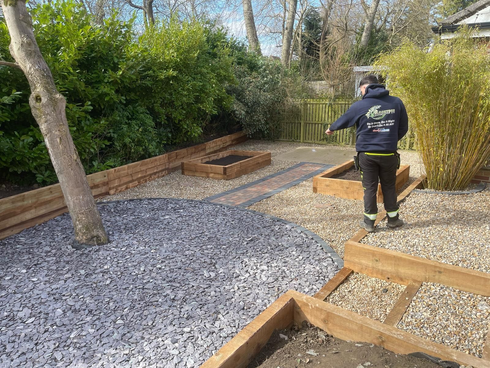 Worker installing gravel in a landscaped garden path with timber edging and bushes nearby