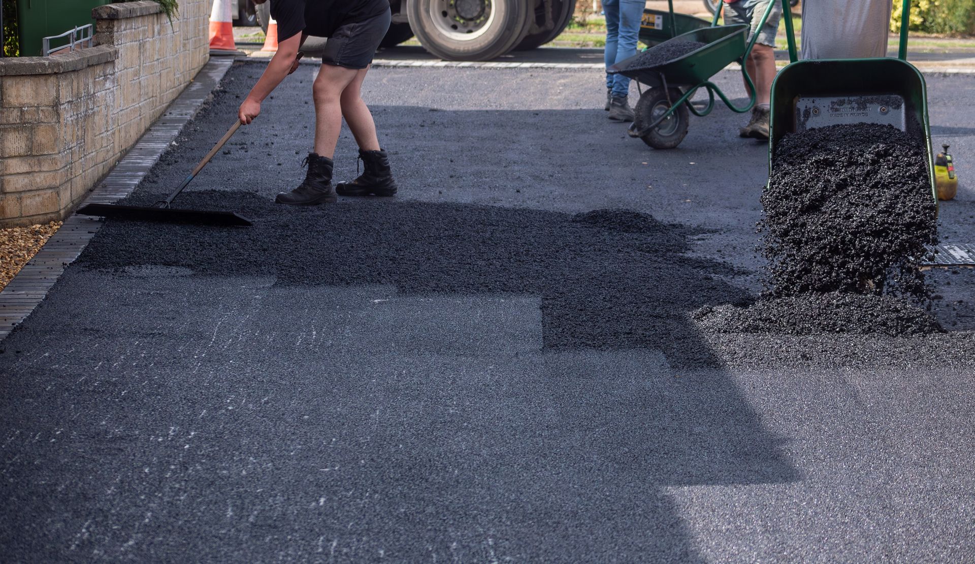 A man is spreading asphalt on a road with a shovel.