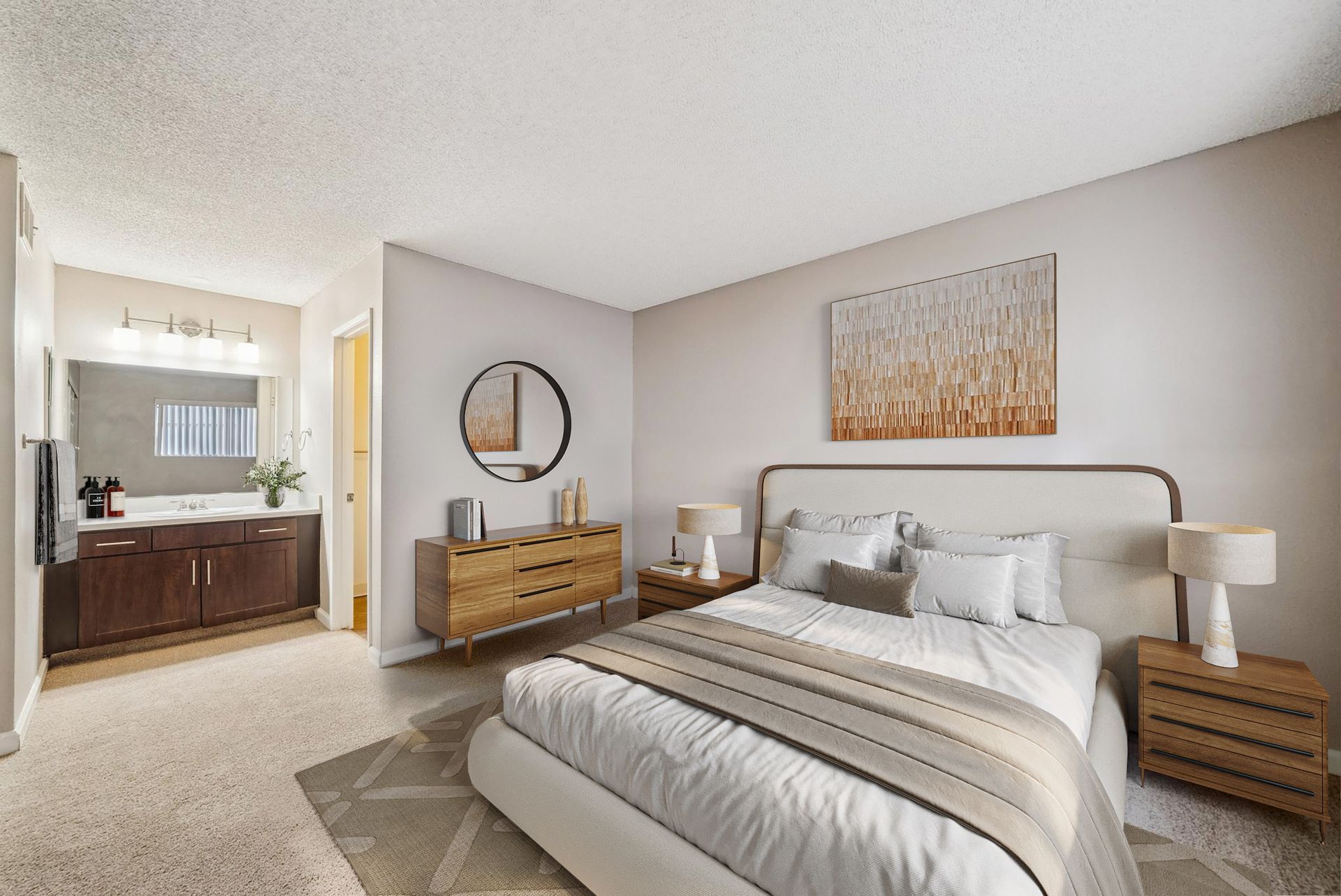 Bedroom with a large bed, two nightstands, dresser with round mirror, and an attached bathroom vanity.