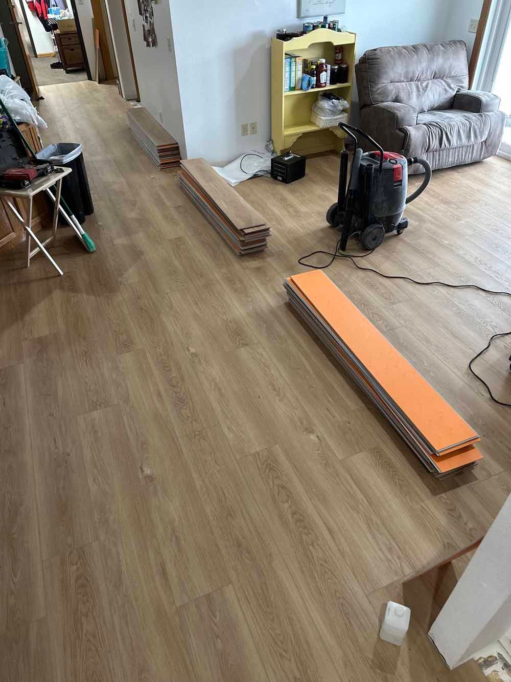 Living room with scattered tools, a vacuum, and an orange floor plank on wood flooring