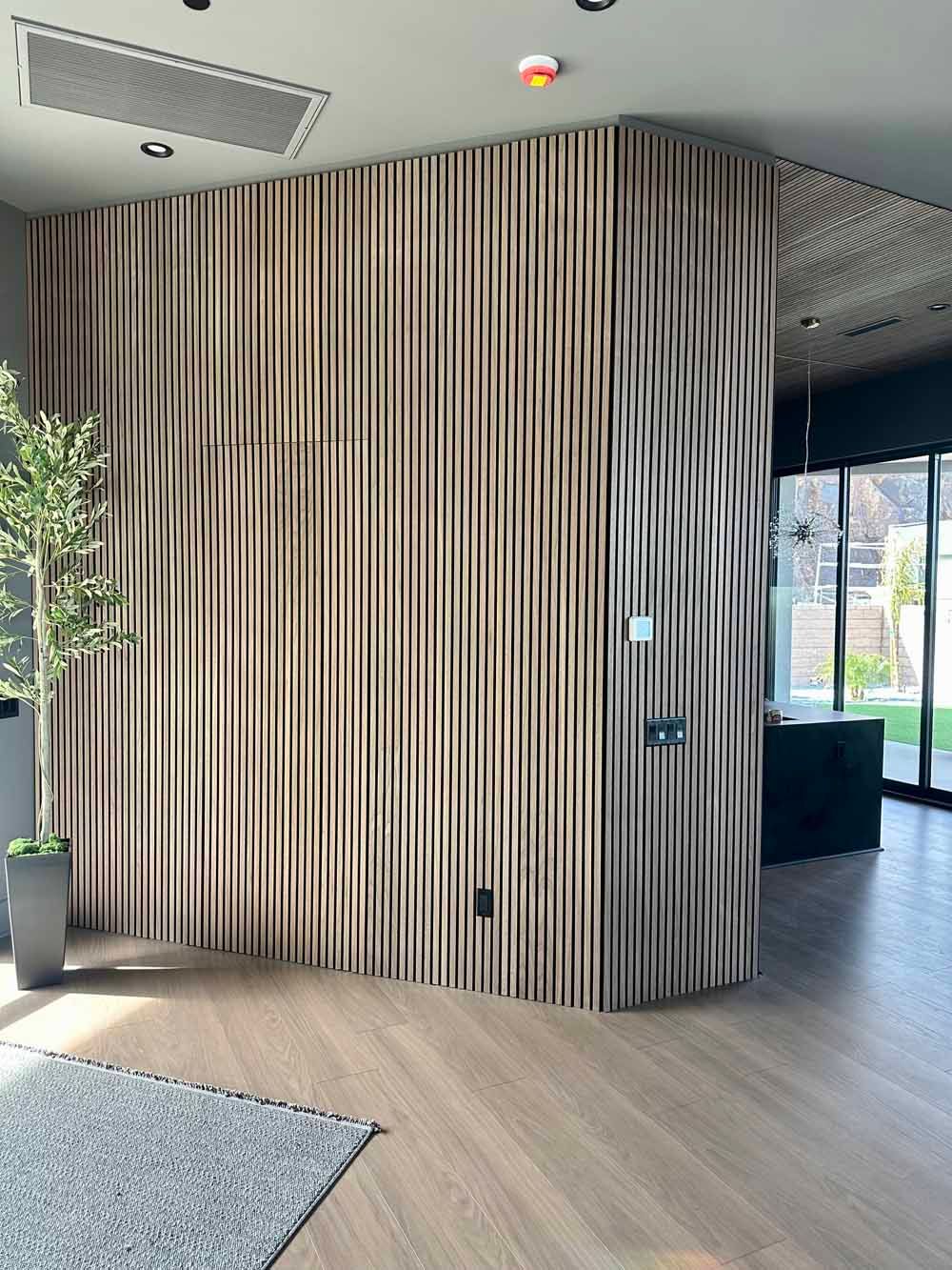 Curved wood-slat wall in a modern lobby with light flooring, a rug, plants, and a bright windowed entrance