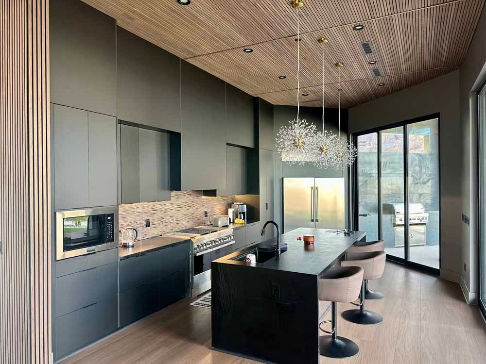 Modern kitchen with dark cabinets, a large island, pendant lights, and floor-to-ceiling glass doors
