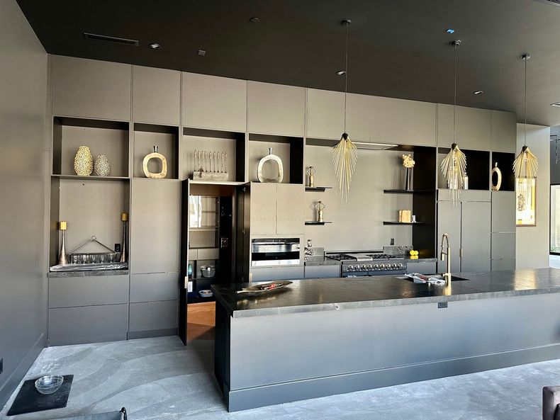 Modern kitchen with matte gray cabinets, dark island, and open shelving under pendant lights.