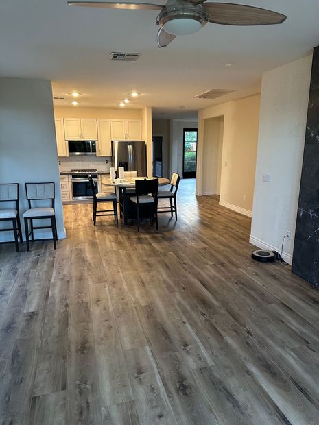 Empty open-plan living room and kitchen with wood floors, ceiling fan, and dining table near the kitchen.