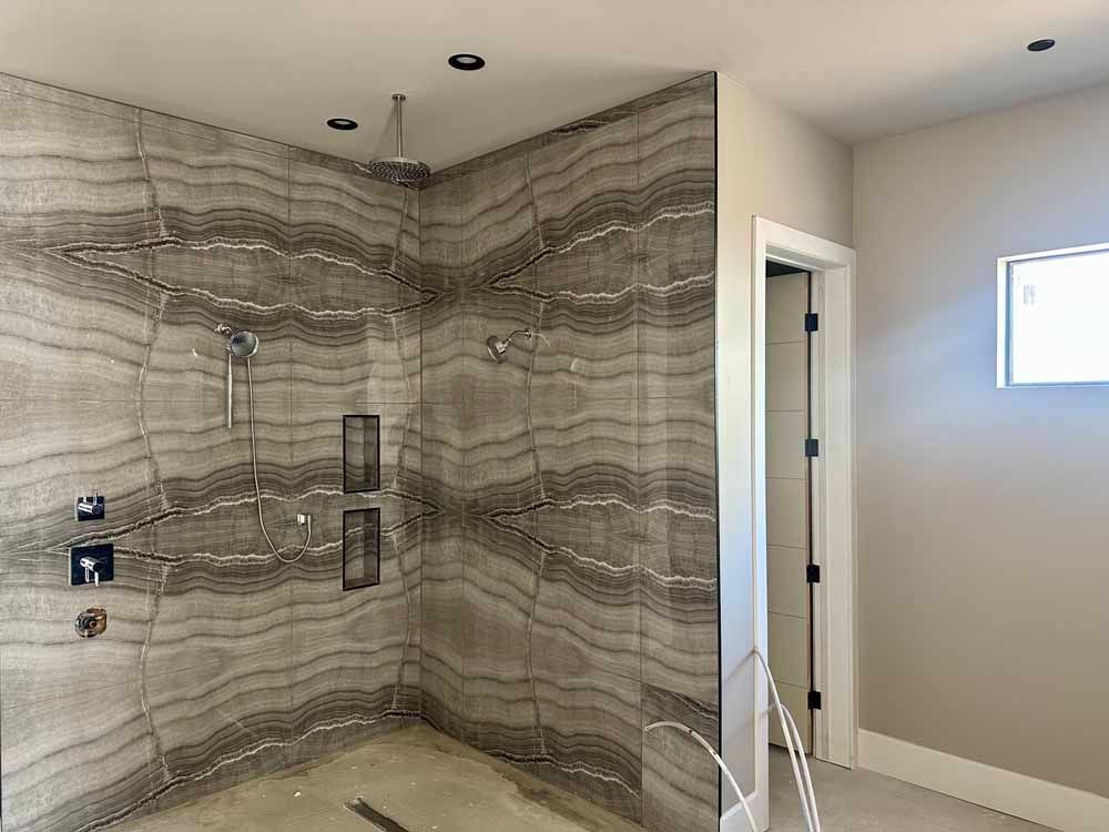Modern bathroom with large marble-tiled shower, glass door, and beige walls