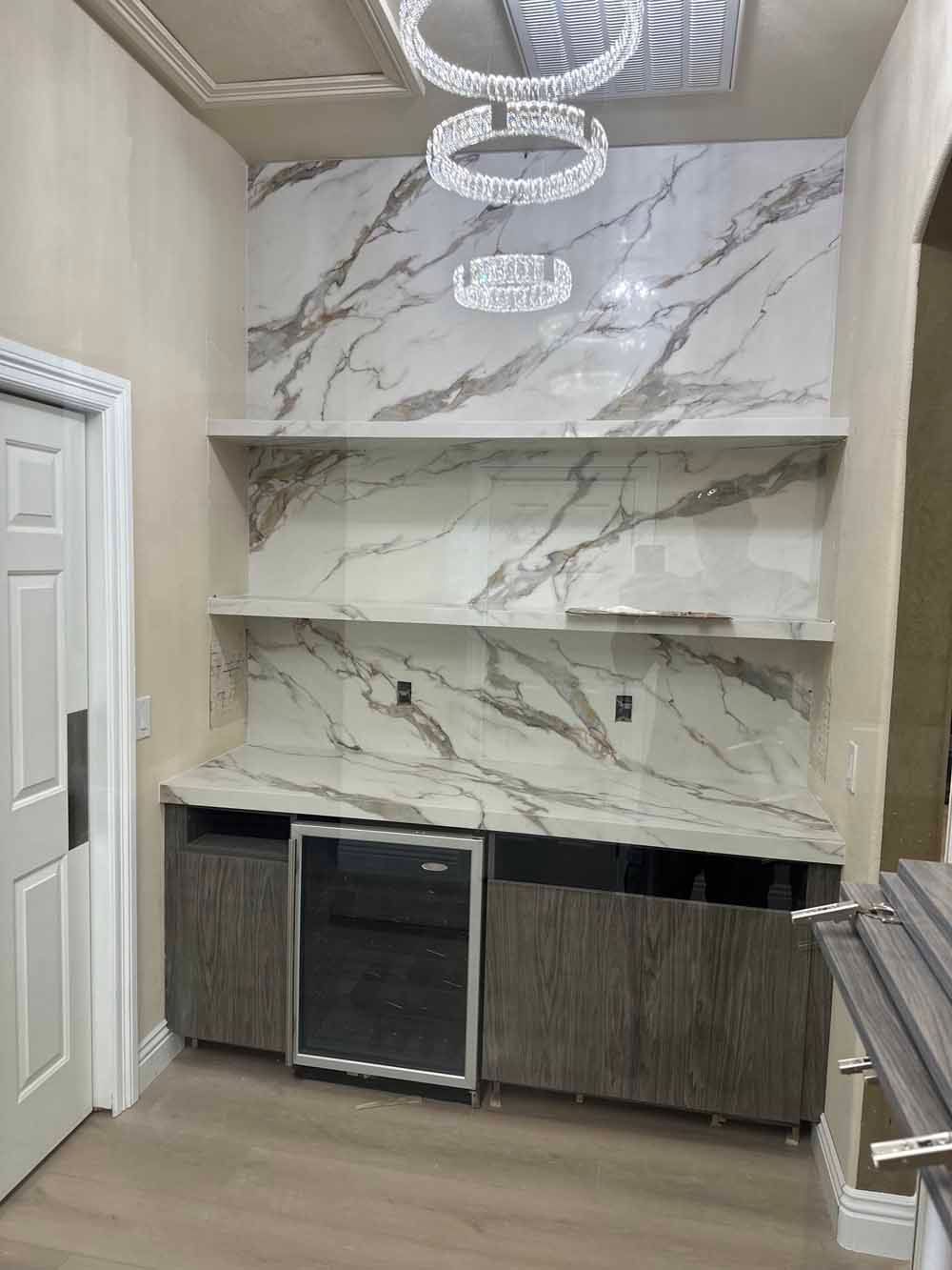 Marble-accented kitchen bar area with under-counter cabinets, mini fridge, and hanging lights