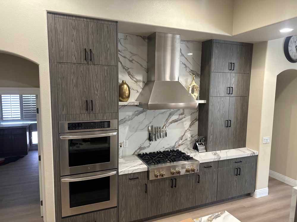 Modern kitchen with dark wood cabinets, stainless steel range hood, and built-in oven.