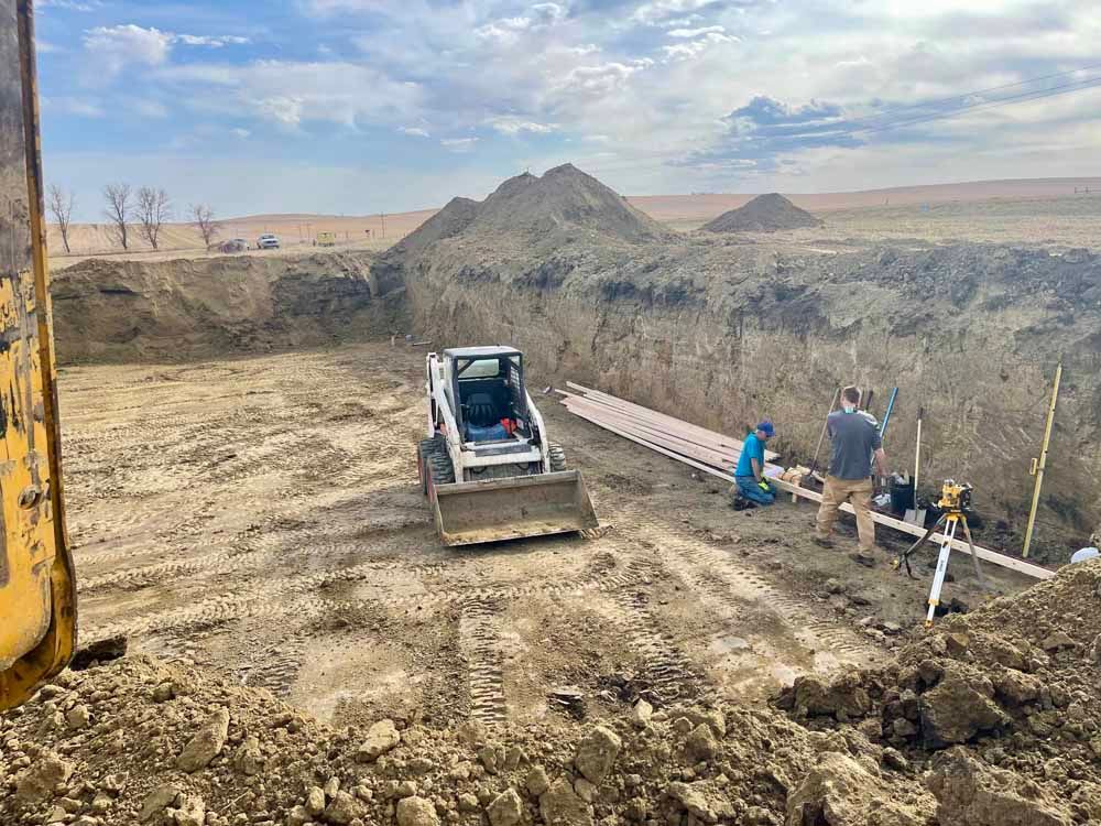 Construction site with excavator, workers, and a large trench in a barren landscape