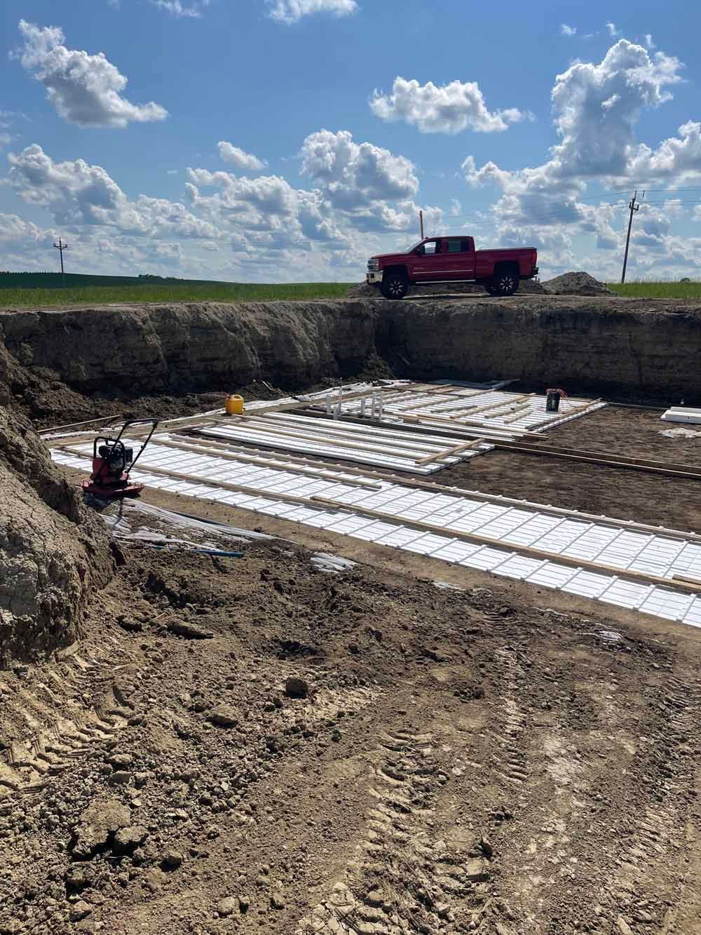Construction site with a red truck, excavator, and white material laid on the ground under a blue sky.