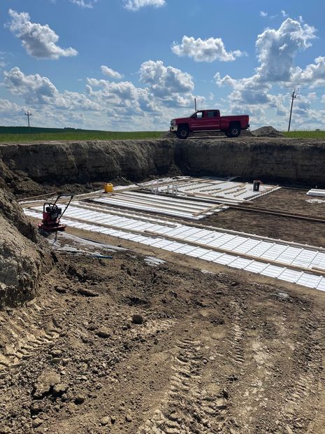 Construction site with red truck, excavated foundation, and workers under a cloudy sky
