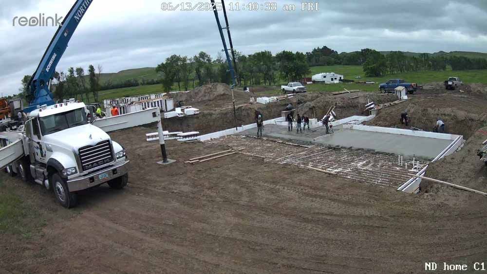 Construction site with a concrete foundation, truck, crane, and workers under overcast skies.