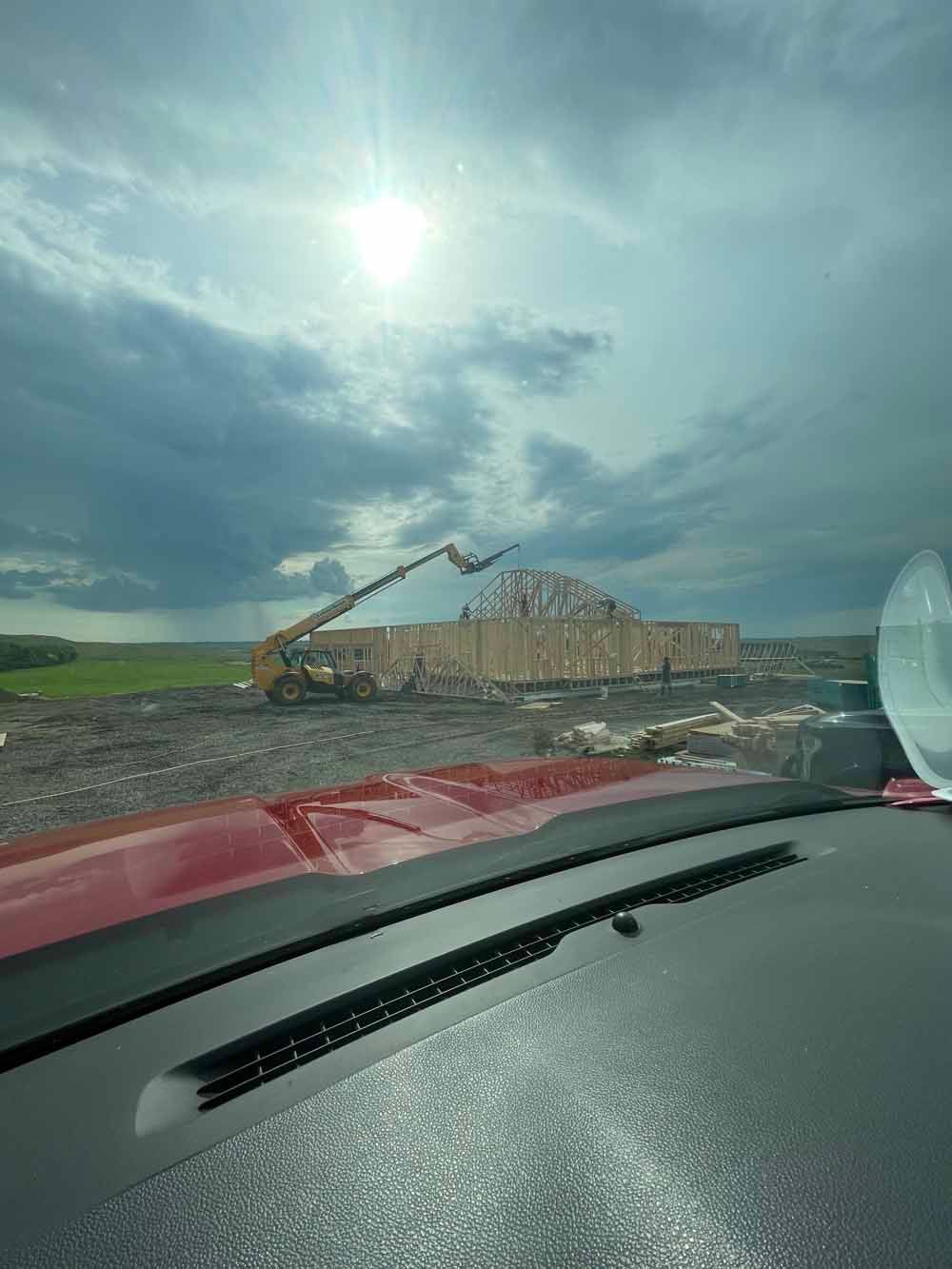 Stormy roadside scene with a red vehicle dashboard, damaged building, and construction equipment under a cloudy sky