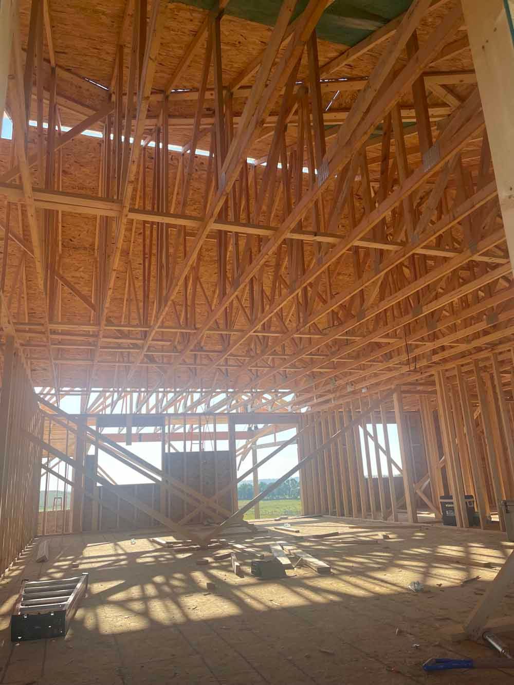 Interior of a timber-framed building under construction with exposed roof trusses and sunlight on the floor