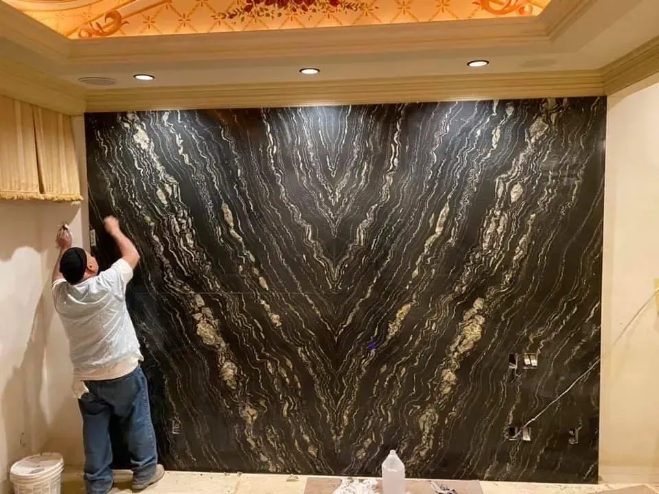 Person installing a large black marble wall panel in a decorated room