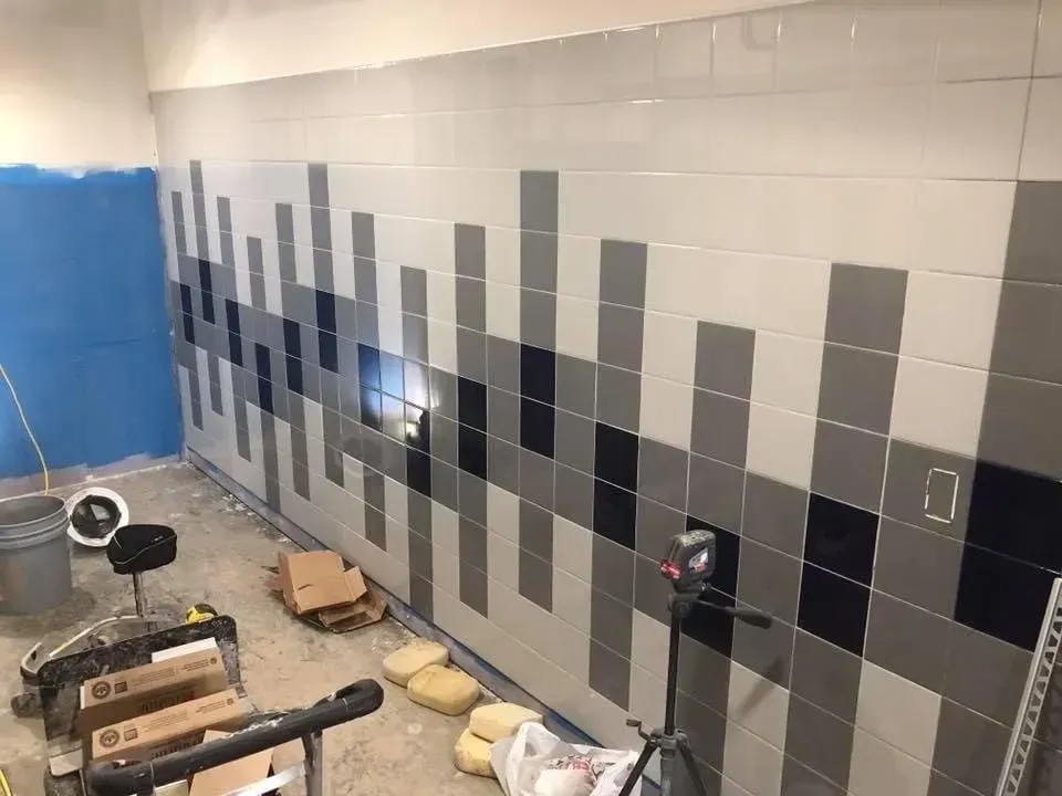 Wall of gray and black tiles in a room, with construction materials and buckets on the floor.