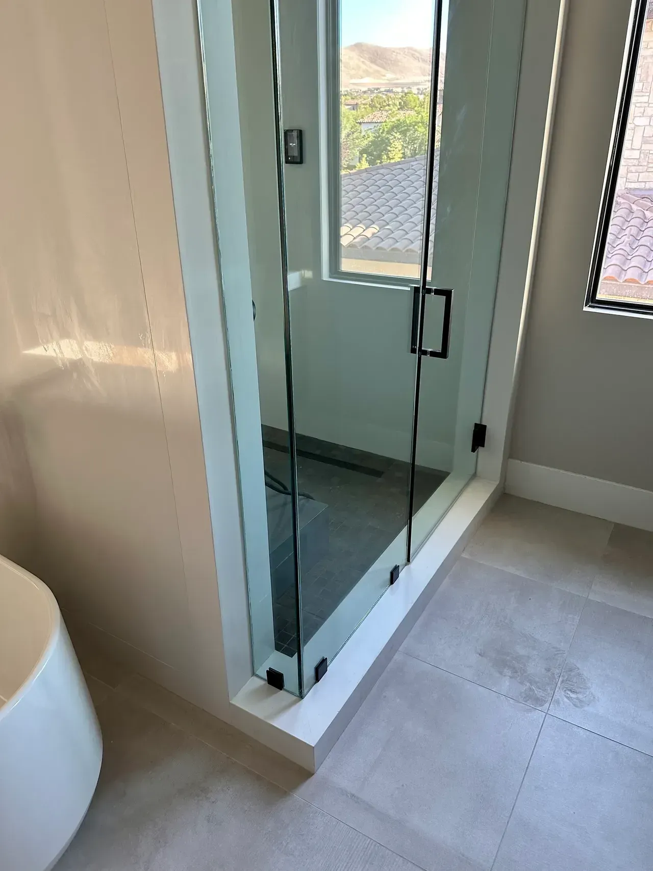 Glass shower enclosure beside a white bathtub in a beige-tiled bathroom