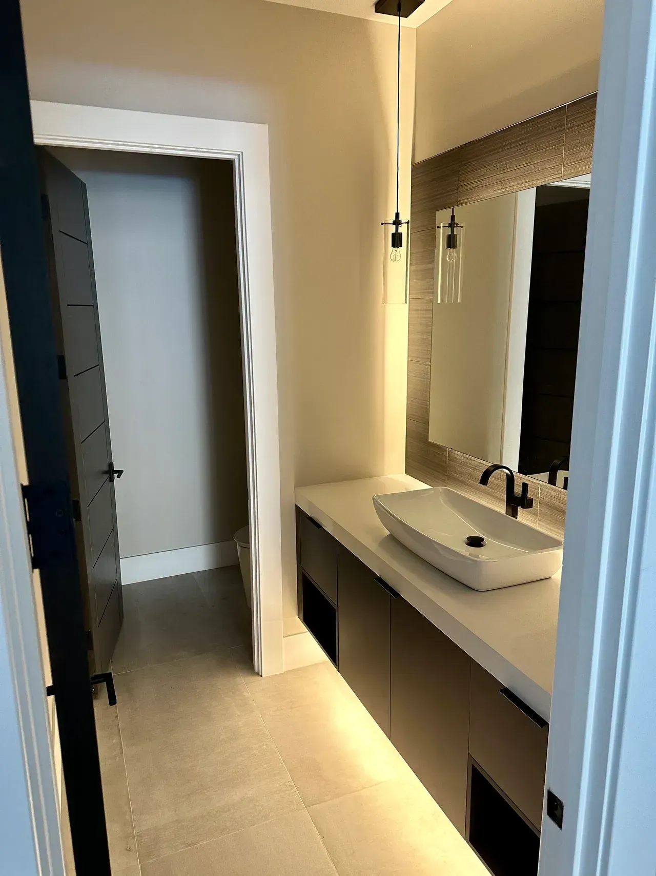 Modern bathroom with a long vanity, sink, mirror, and open doorway to a hallway.