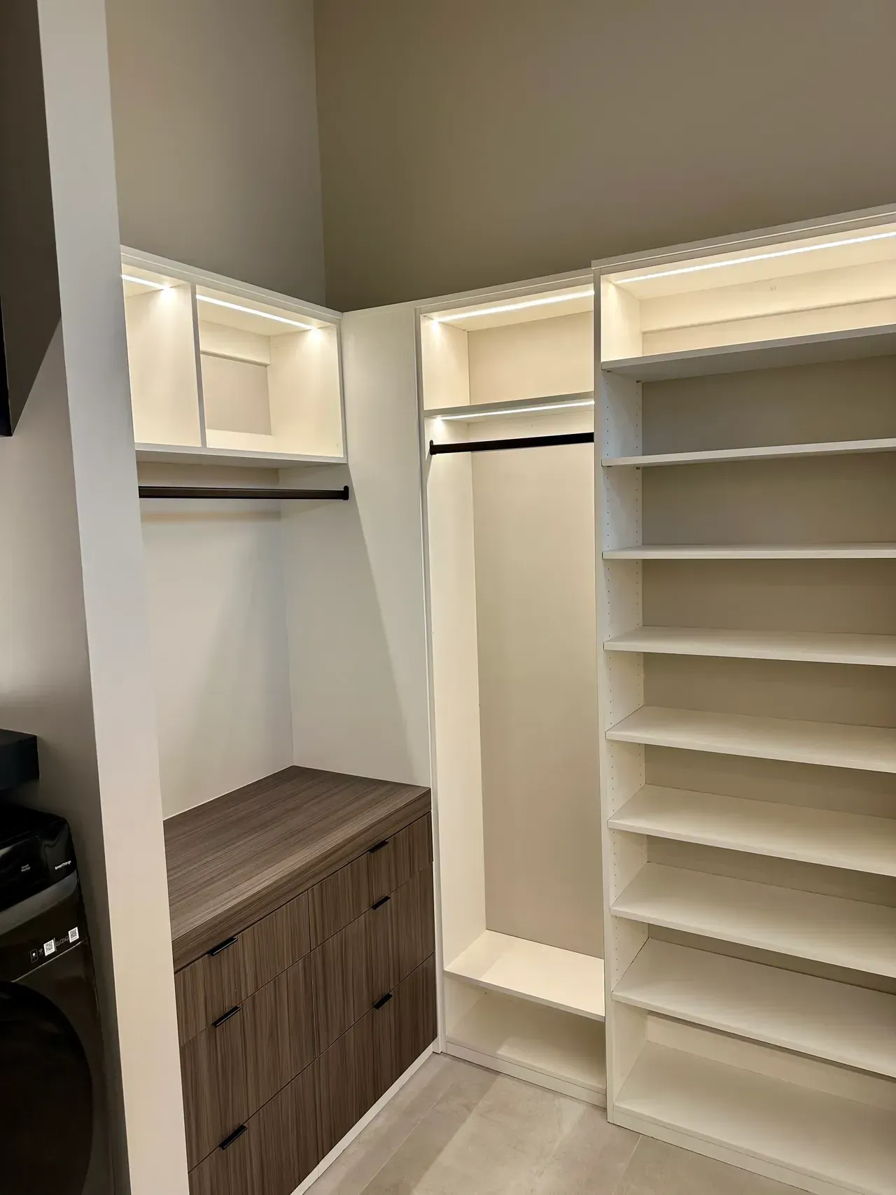 Empty walk-in closet with white shelves and hanging rods, plus a dark wood drawer cabinet.