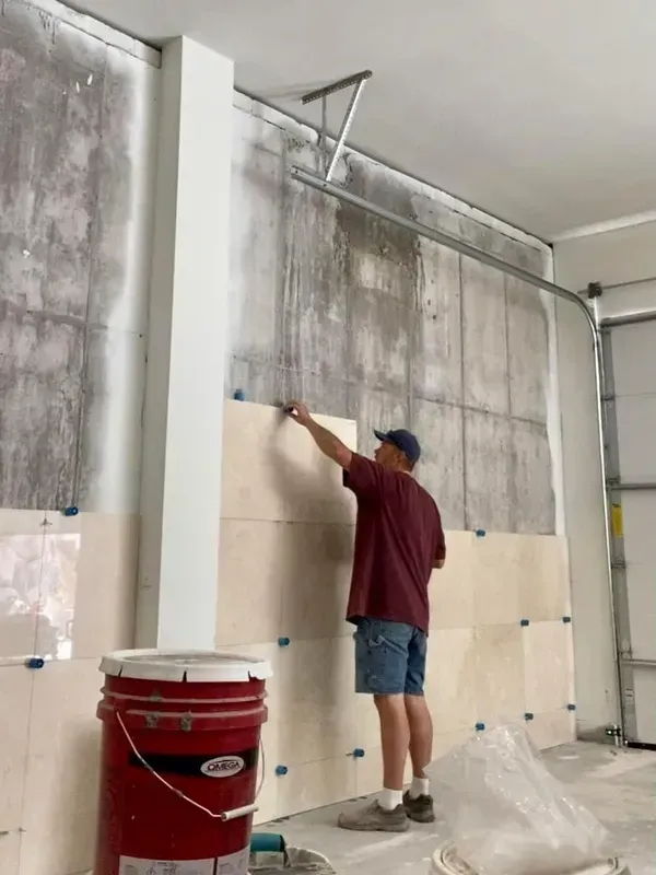 Person painting a tall white column on a concrete wall in an unfinished room