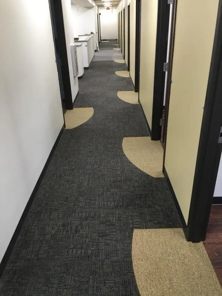 Narrow office hallway with dark carpet, beige door mats, and open doors along both sides.