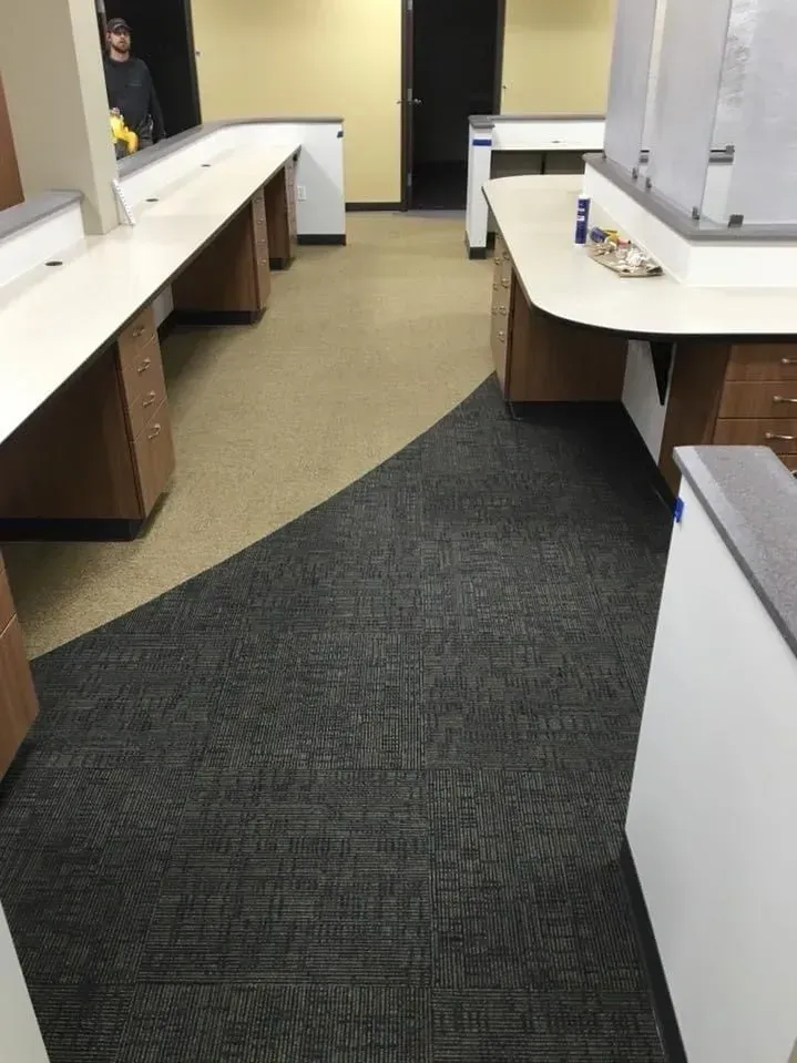 Office hallway with white counters, beige walls, and a dark carpet runner leading to a doorway.
