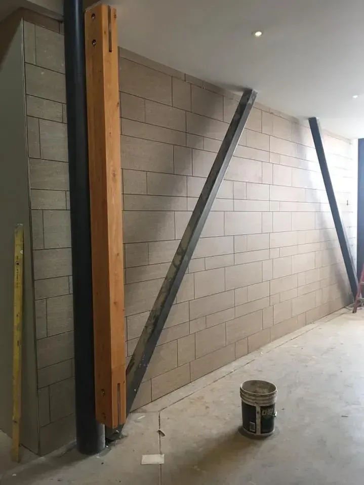 Unfinished interior wall with cinder blocks, diagonal braces, exposed wood studs, and a paint can on the floor