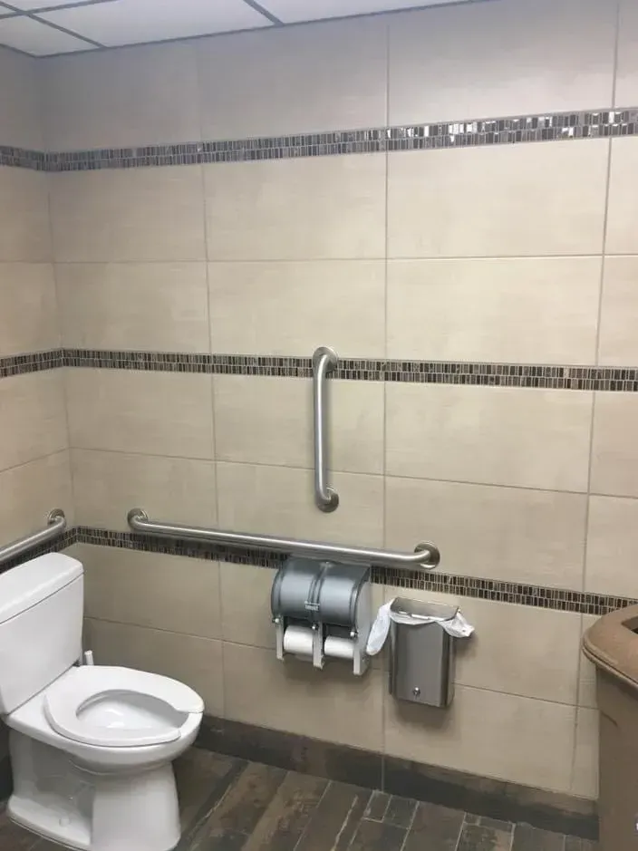 Accessible restroom with toilet, grab bars, and toilet paper holder against beige tiled wall