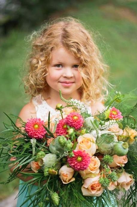 Jong kind met een groot boeket roze, witte en perzikkleurige bloemen in een tuin.