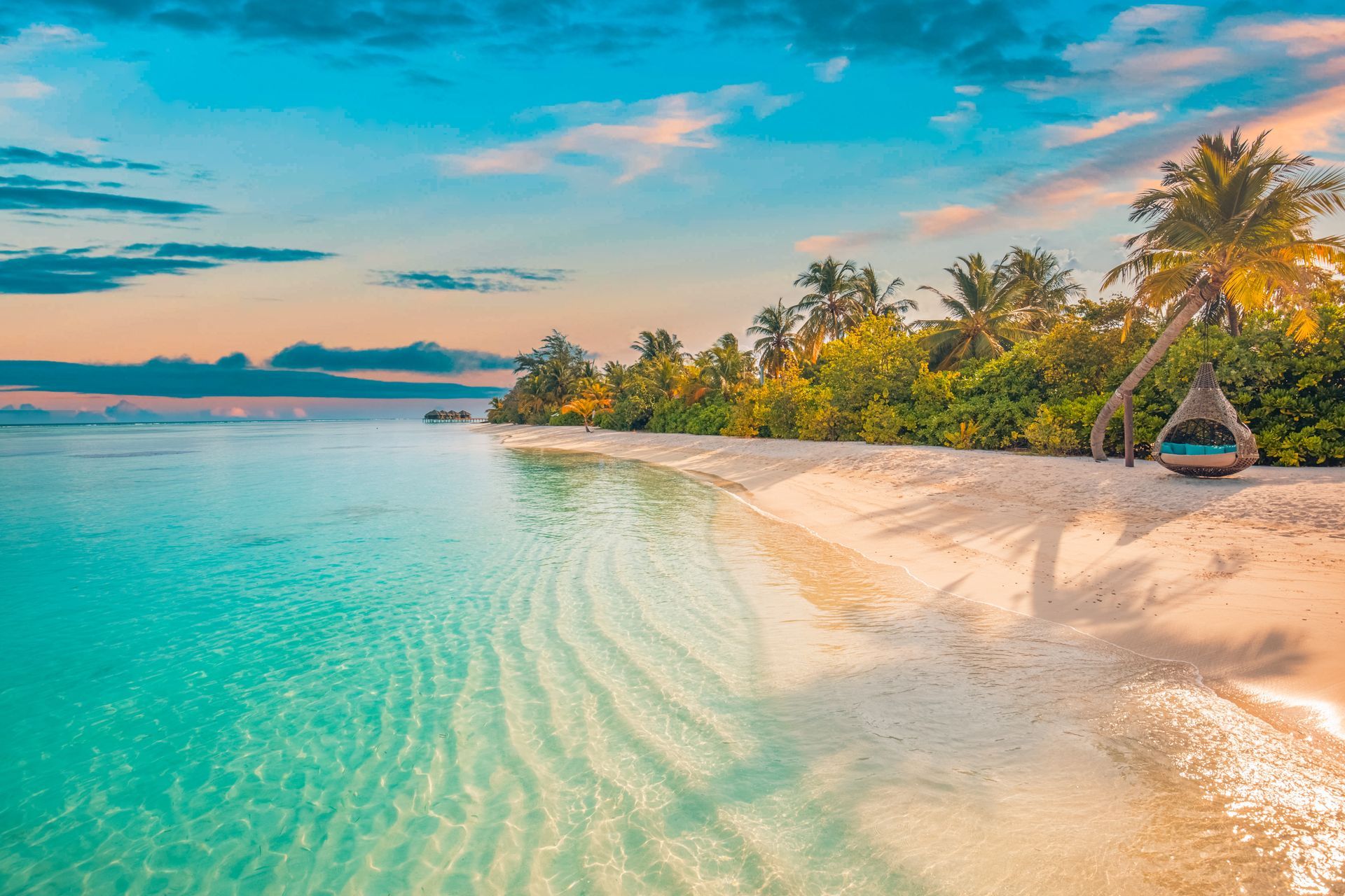 Tropical beach with turquoise water, white sand, palm trees, and a small hut at sunset