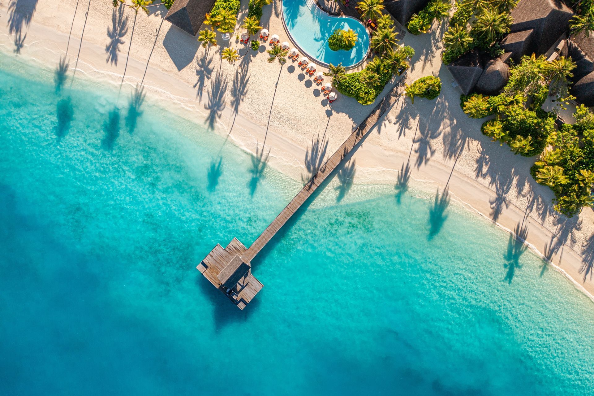 Aerial view of a tropical beach with turquoise water, a wooden pier, and palm trees along the shore