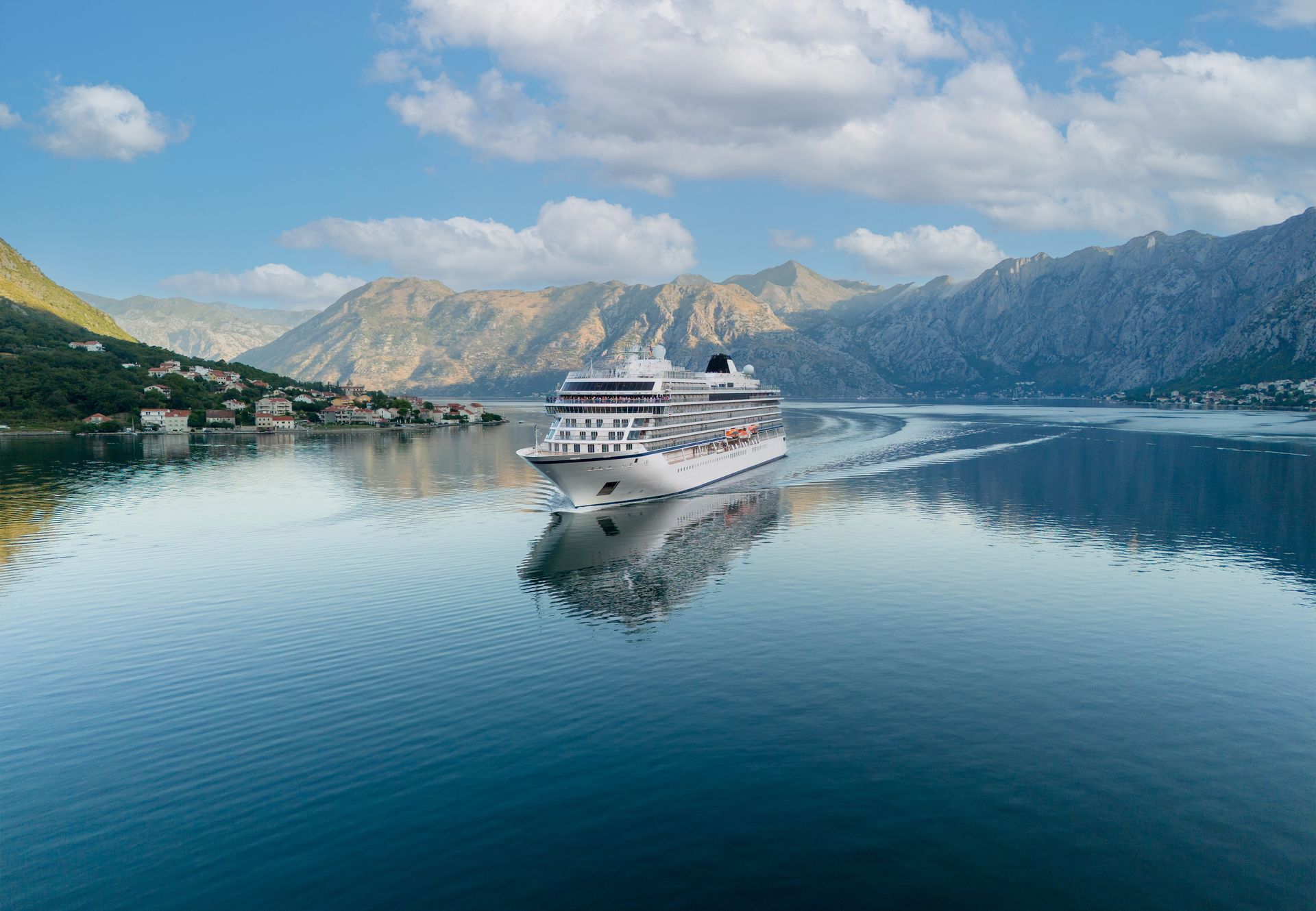 White cruise ship on calm blue water with mountain reflections under a partly cloudy sky