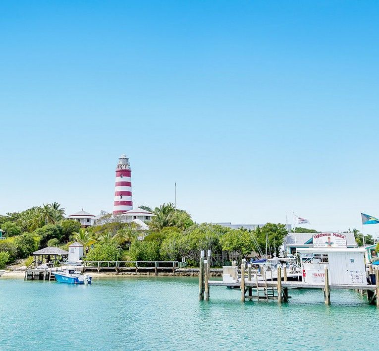 Red-and-white striped lighthouse on a tropical shoreline with turquoise water and docks under a clear blue sky