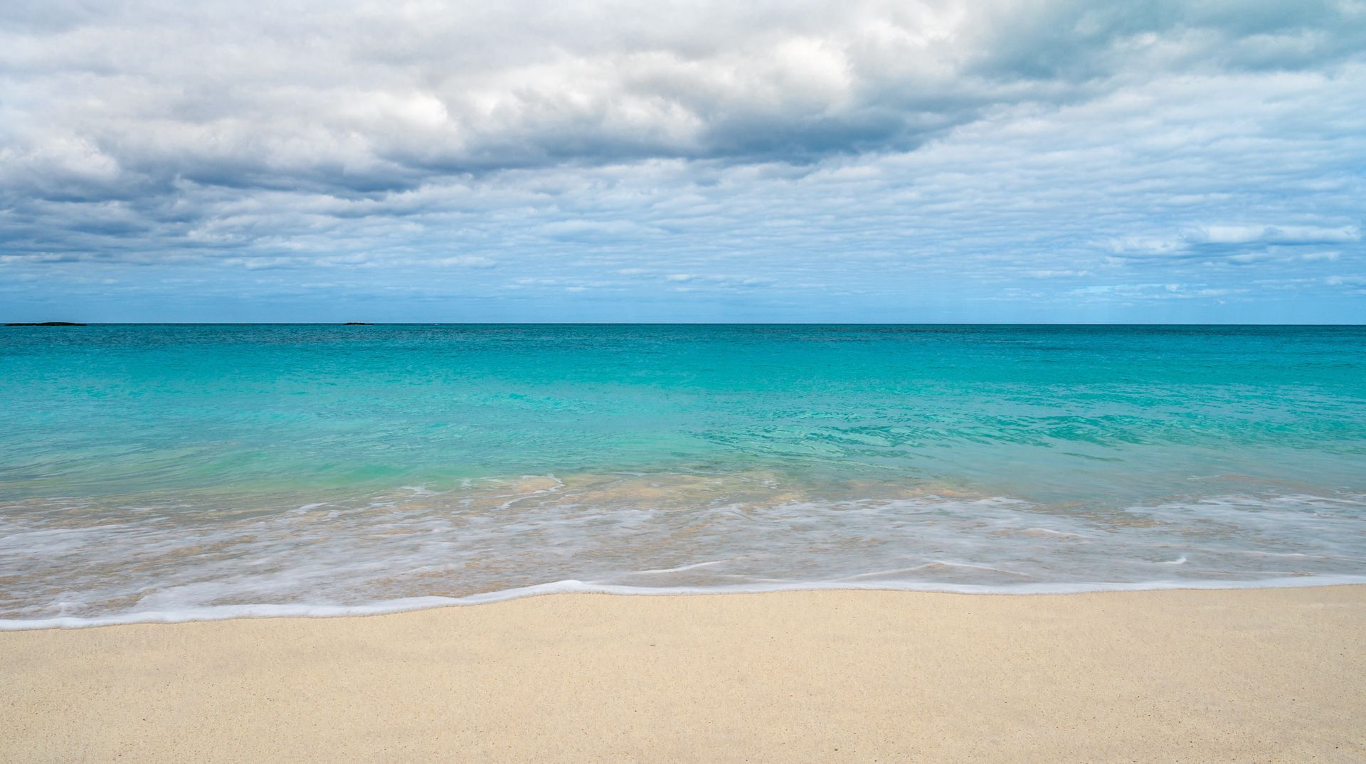 Calm turquoise ocean meeting a sandy beach under a cloudy sky