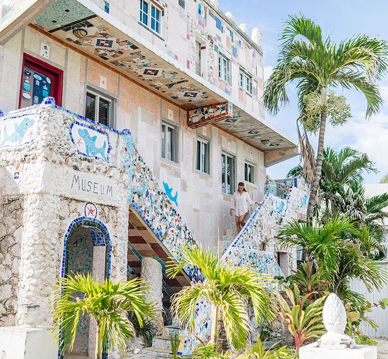 Colorful mosaic building with stairs, palm trees, and a person standing on the balcony